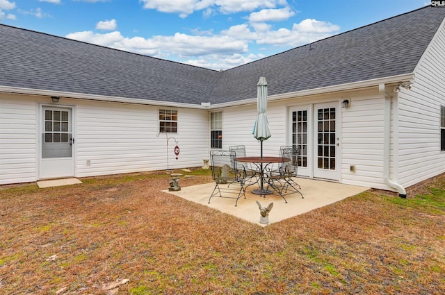 rear view of property with a shingled roof, a lawn, and a patio