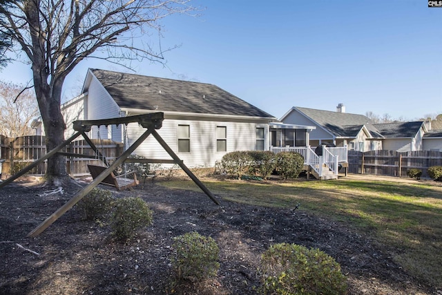 back of house with a deck, a playground, a shingled roof, fence, and a lawn