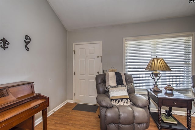 living area with vaulted ceiling, baseboards, and wood finished floors
