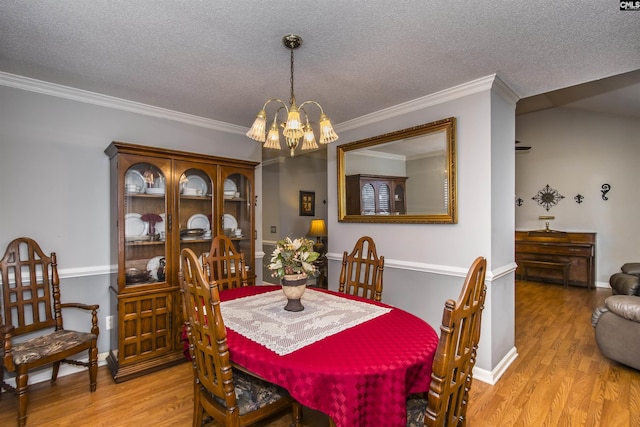 dining space featuring ornamental molding, a notable chandelier, light wood-style flooring, and a textured ceiling