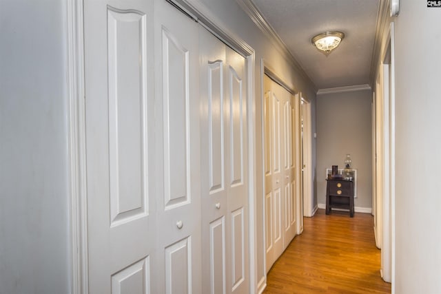 corridor featuring a textured ceiling, light wood finished floors, baseboards, and crown molding