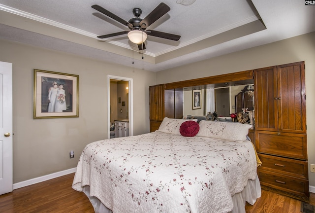 bedroom with a tray ceiling, dark wood-style flooring, and baseboards