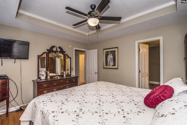 bedroom featuring a textured ceiling, wood finished floors, a raised ceiling, and crown molding