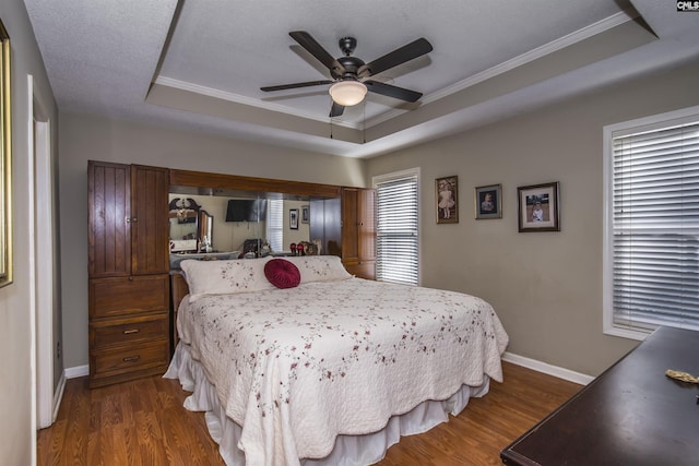 bedroom with ornamental molding, a tray ceiling, dark wood finished floors, and baseboards