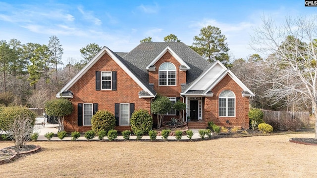 traditional-style home featuring roof with shingles, a front lawn, and brick siding