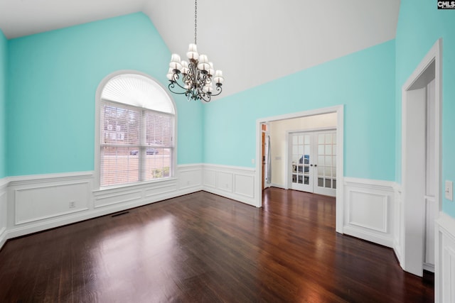 unfurnished dining area featuring a wainscoted wall, wood finished floors, visible vents, vaulted ceiling, and an inviting chandelier