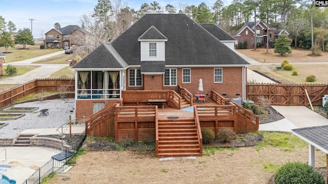 rear view of house featuring brick siding, a shingled roof, stairway, a sunroom, and a fenced backyard