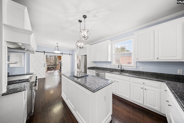 kitchen with a barn door, ornamental molding, a center island, stainless steel appliances, and a sink