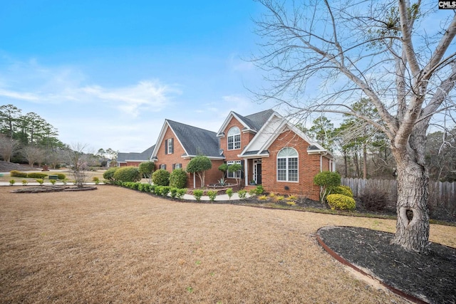 view of front facade featuring brick siding, fence, and a front lawn