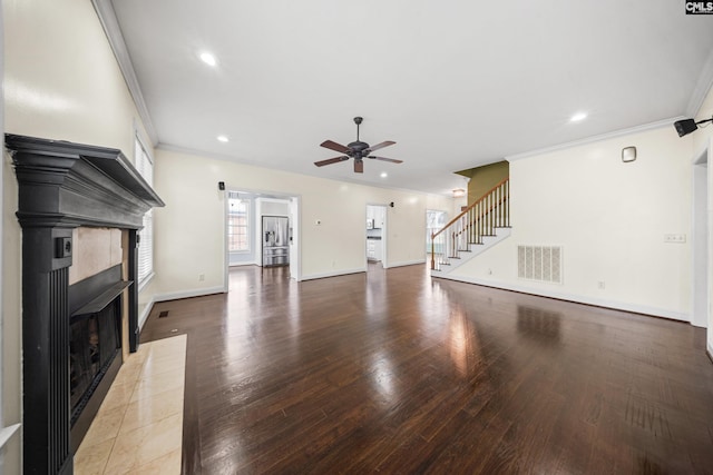 unfurnished living room featuring wood finished floors, a fireplace with flush hearth, visible vents, ornamental molding, and stairway