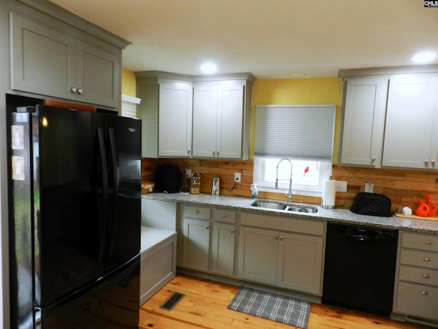 kitchen featuring light wood-style floors, a sink, black appliances, and light stone countertops