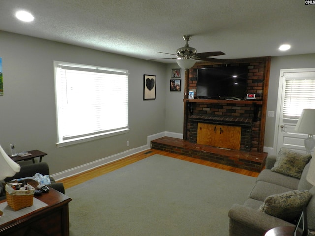 living room featuring a textured ceiling, a fireplace, wood finished floors, a ceiling fan, and baseboards