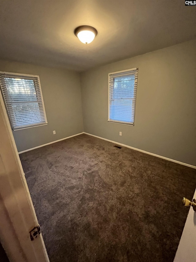 unfurnished room with visible vents, dark carpet, and baseboards