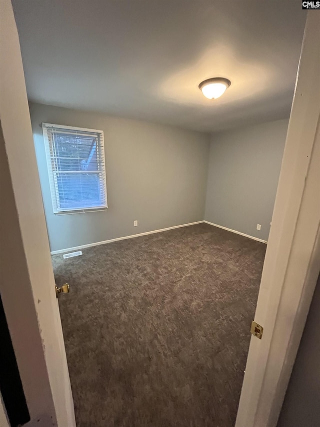 unfurnished room with visible vents, dark carpet, and baseboards