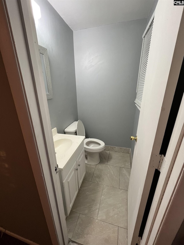 half bath with marble finish floor, vanity, and toilet