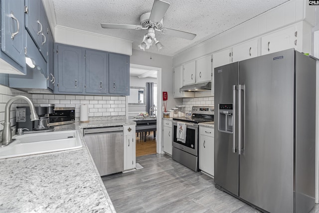 kitchen featuring under cabinet range hood, stainless steel appliances, a sink, a ceiling fan, and light countertops