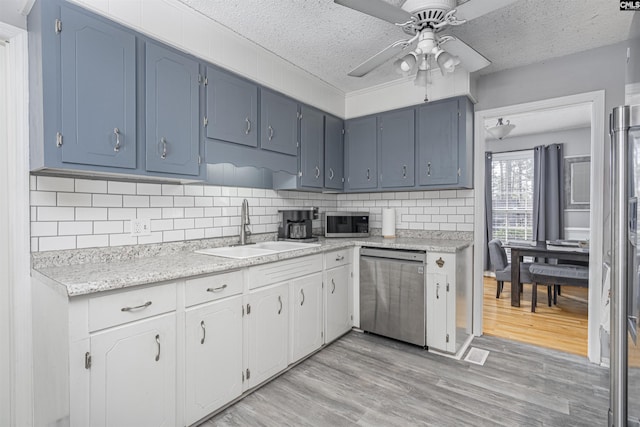 kitchen featuring a textured ceiling, stainless steel appliances, a sink, light wood-style floors, and white cabinets