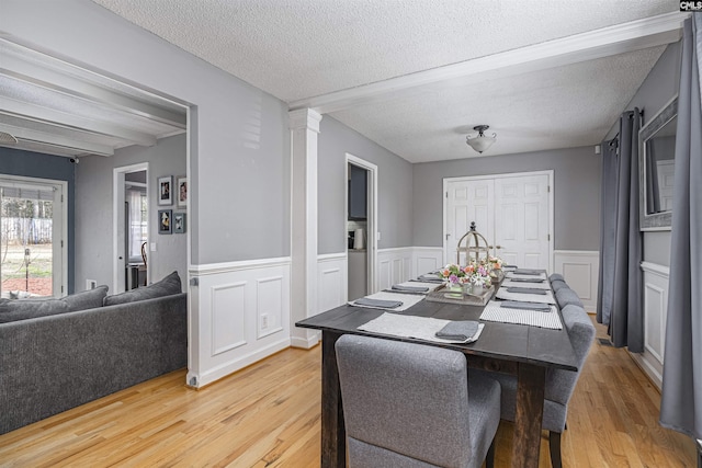 dining area featuring decorative columns, a textured ceiling, wood finished floors, and wainscoting