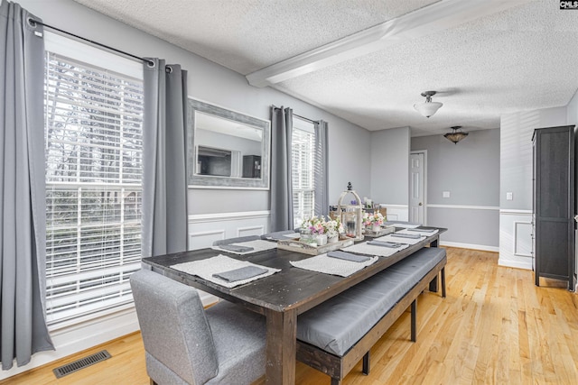 dining area with light wood-style flooring, visible vents, a textured ceiling, and wainscoting