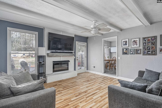 living area with a textured ceiling, a fireplace, wood finished floors, baseboards, and beamed ceiling