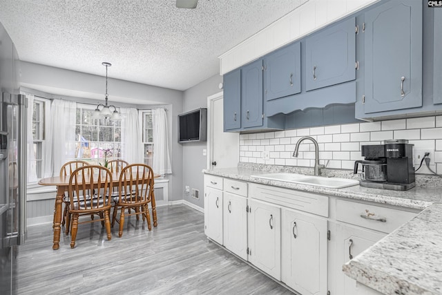 kitchen with decorative backsplash, light wood-style flooring, hanging light fixtures, white cabinetry, and a sink