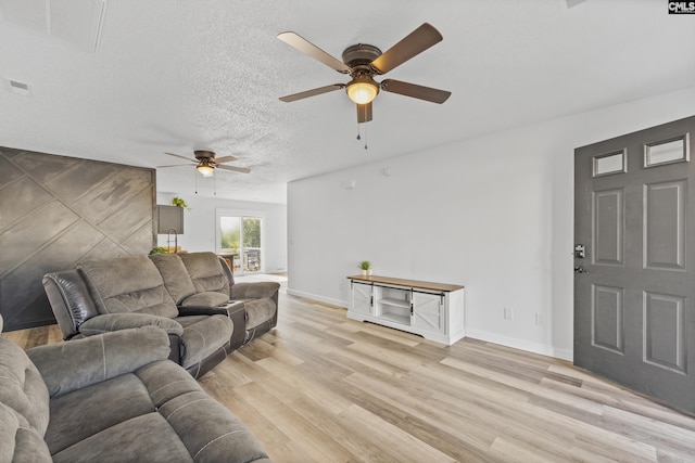 living area featuring visible vents, light wood-style flooring, a ceiling fan, a textured ceiling, and baseboards