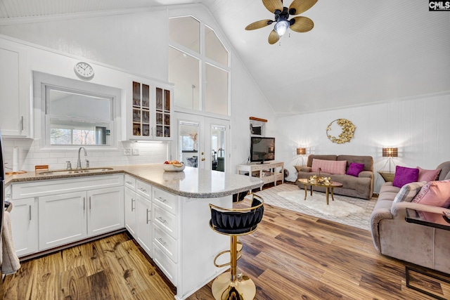 kitchen featuring glass insert cabinets, open floor plan, a peninsula, white cabinetry, and a sink