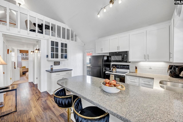 kitchen with white cabinets, glass insert cabinets, vaulted ceiling, black appliances, and a sink