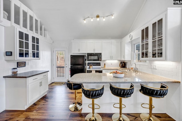 kitchen featuring white cabinetry, vaulted ceiling, light stone countertops, black appliances, and glass insert cabinets