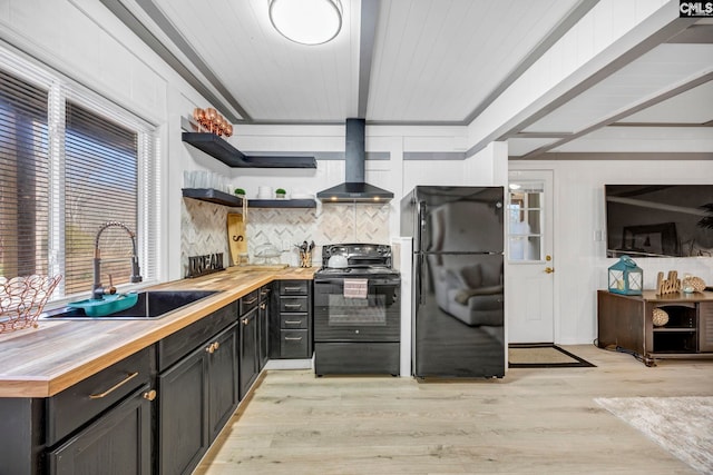 kitchen featuring light wood finished floors, wooden counters, a sink, black appliances, and wall chimney exhaust hood