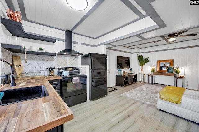 kitchen featuring open shelves, wood counters, black appliances, light wood-type flooring, and wall chimney exhaust hood