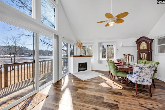 sunroom / solarium featuring a water view, vaulted ceiling, a ceiling fan, and a glass covered fireplace