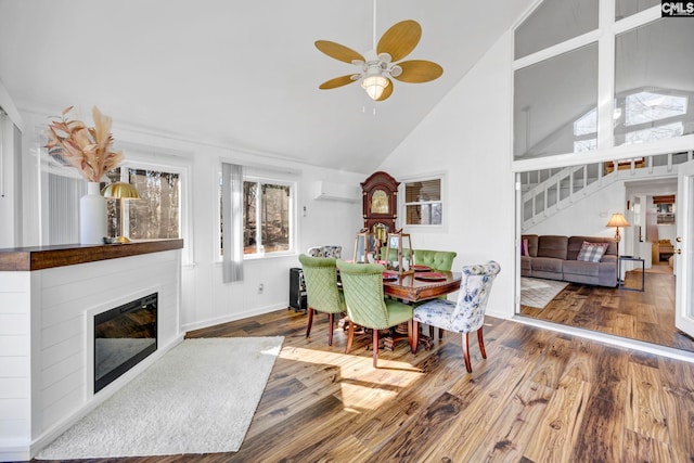 dining space featuring a wall unit AC, a glass covered fireplace, ceiling fan, wood finished floors, and stairs