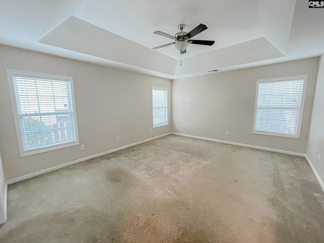 empty room with light carpet, ceiling fan, baseboards, and a raised ceiling