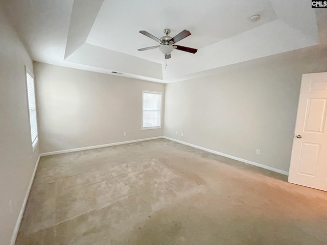 unfurnished room with light colored carpet, a ceiling fan, visible vents, baseboards, and a raised ceiling