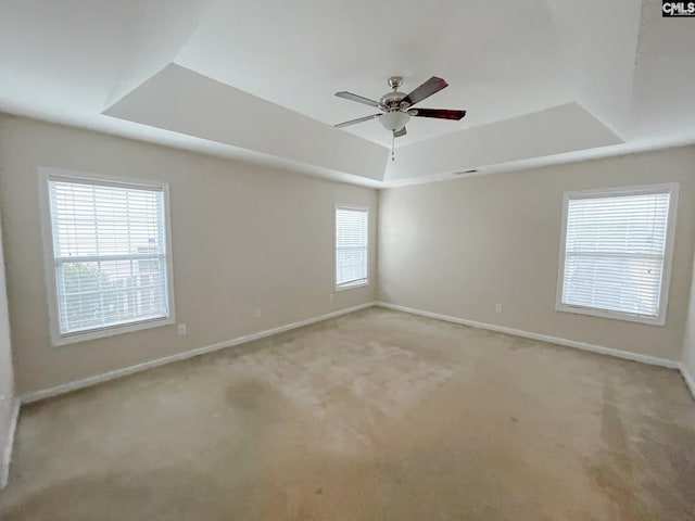 unfurnished room with a tray ceiling, light colored carpet, ceiling fan, and baseboards