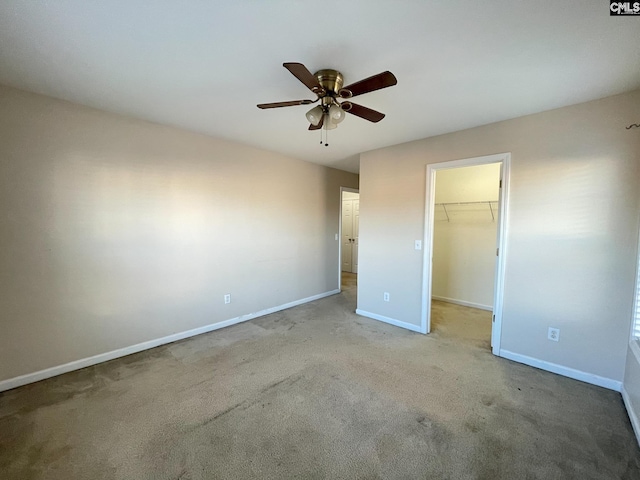 unfurnished bedroom with a closet, a spacious closet, light carpet, ceiling fan, and baseboards