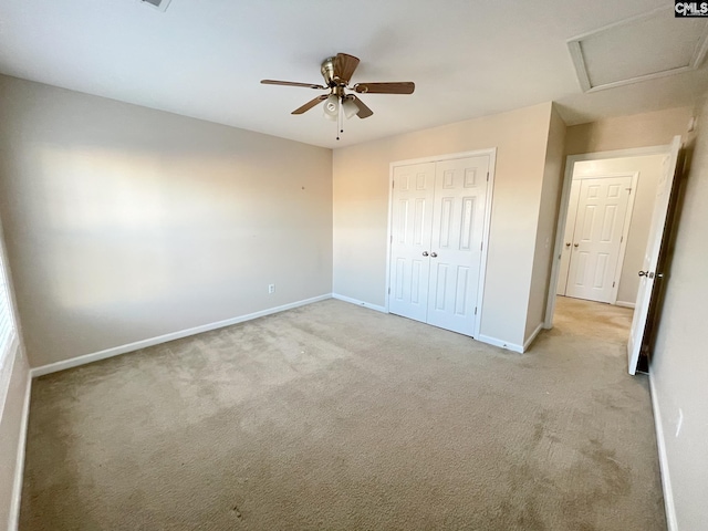 unfurnished bedroom with light carpet, attic access, baseboards, a ceiling fan, and a closet