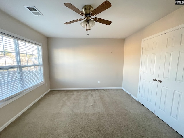 spare room with light carpet, baseboards, visible vents, and a ceiling fan