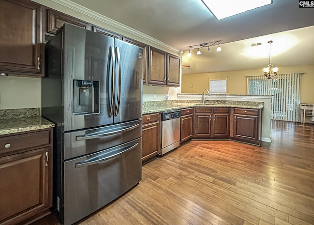 kitchen featuring stainless steel appliances, a peninsula, a sink, light wood-style floors, and decorative light fixtures