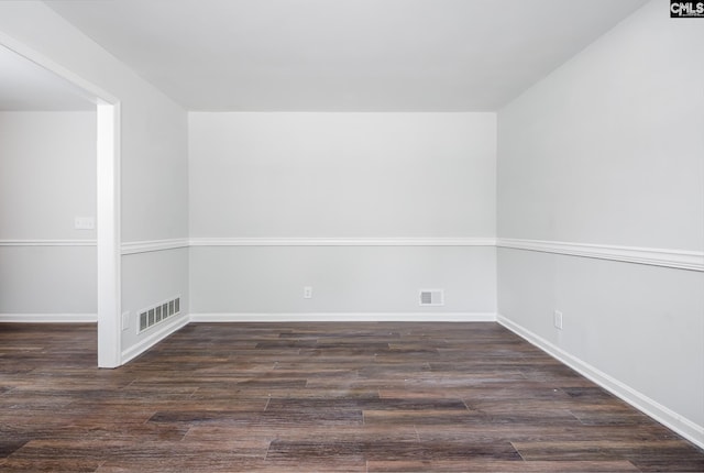 empty room with dark wood-style flooring, visible vents, and baseboards