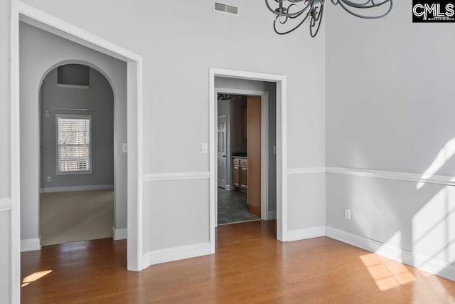 interior space with arched walkways, visible vents, an inviting chandelier, and wood finished floors