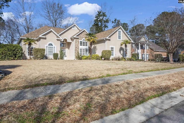 traditional-style house featuring a front yard, stone siding, and stucco siding