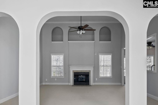 unfurnished living room featuring baseboards, a tiled fireplace, a ceiling fan, and light colored carpet