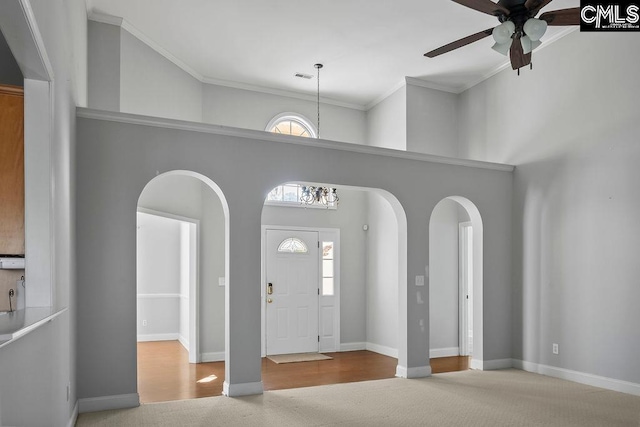 entryway with baseboards, arched walkways, ceiling fan, a high ceiling, and crown molding