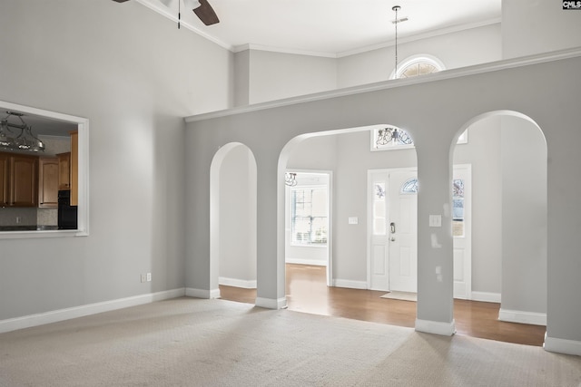 foyer with a ceiling fan, arched walkways, crown molding, and a towering ceiling