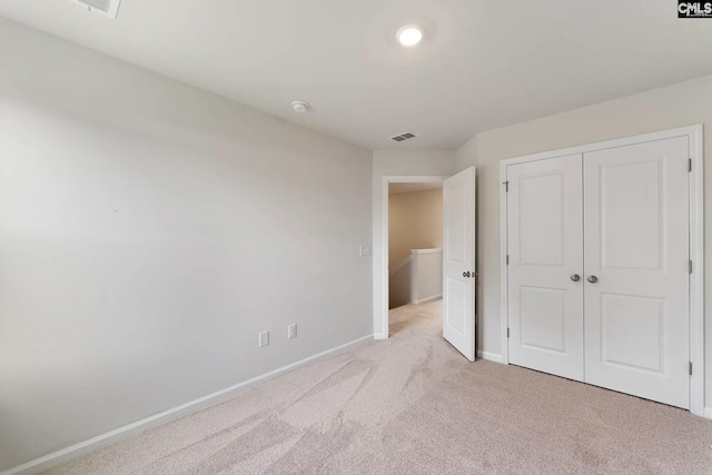 unfurnished bedroom featuring light colored carpet, a closet, visible vents, and baseboards