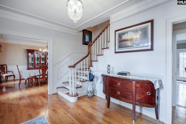 stairs with a decorative wall, a wainscoted wall, a notable chandelier, wood finished floors, and ornamental molding