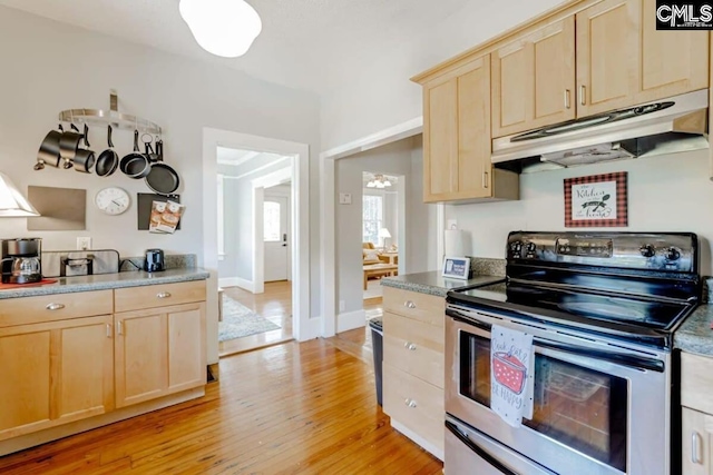 kitchen featuring light brown cabinetry, dark countertops, stainless steel range with electric stovetop, and under cabinet range hood