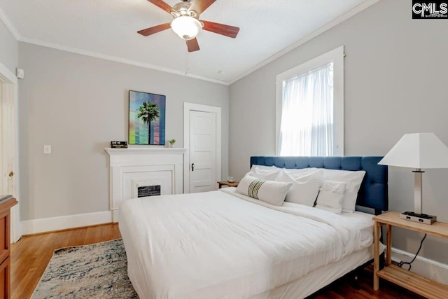 bedroom with baseboards, a fireplace, wood finished floors, and crown molding